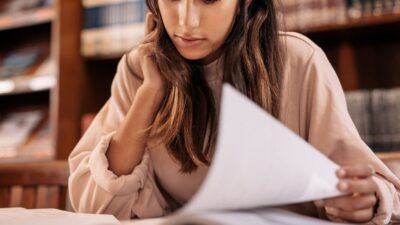 Studentka planująca indywidualny tok studiów przy biurku uniwersyteckiej biblioteki, z rozłożonymi książkami.