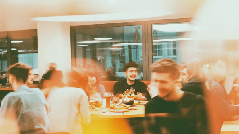 Grupa studentów spożywa niedrogie posiłki w przytulnej warszawskiej restauracji, ciesząc się jedzeniem i atmosferą przy wspólnym stole