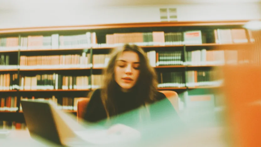 Studentka pracująca nad bibliografią swojej pracy naukowej w bibliotece uniwersyteckiej, otoczona książkami i notatkami