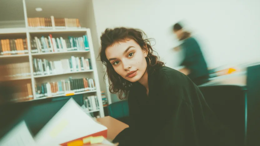 Studentka tworząca przypisy do pracy naukowej w bibliotece uniwersyteckiej