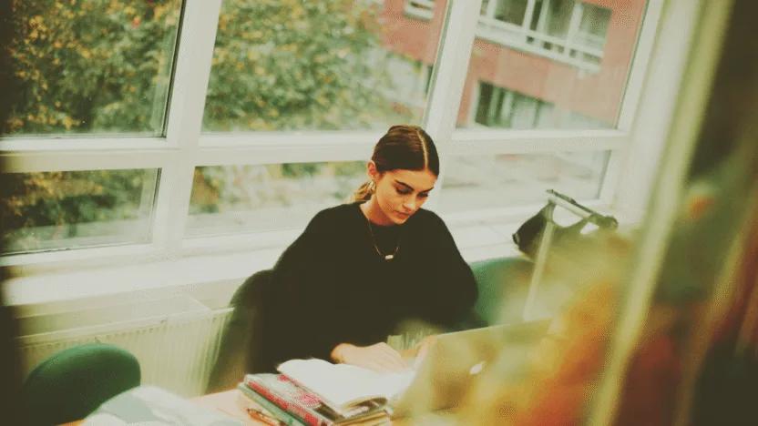 Kryminologia studia - studentka podczas nauki w bibliotece uniwersyteckiej z podręcznikami do kryminologii